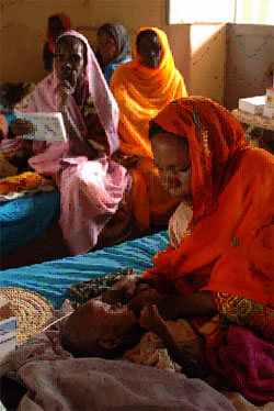 Malik, a severely malnourished one-year-old boy, is comforted by his mother, Hawa, in a UNICEF-supported therapeutic feeding centre at the El Fasher Teaching Hospital in El Fasher, capital of North Darfur. Several other women are visible behind them. Courtesy UNICEF.